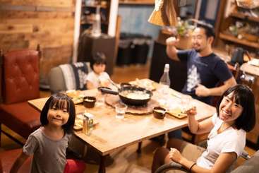The image shows a family dining table with a family of four, featuring a mother, father, and two children, posing for a photo, with a table and chairs in the background.