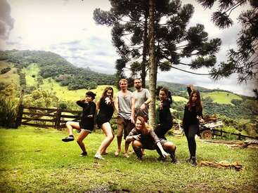 The image depicts a group of seven individuals posing for a photo in a picturesque outdoor setting, surrounded by lush greenery and rolling hills.