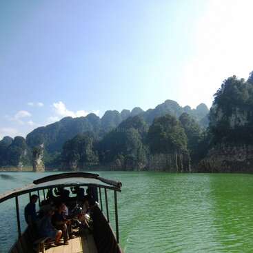 The image depicts a serene scene of a boat on a tranquil body of water, surrounded by majestic mountains and lush greenery under a clear blue sky.