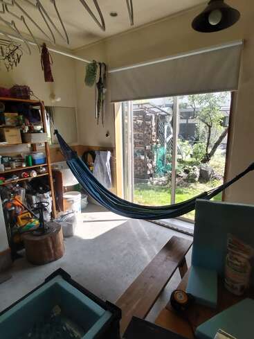This cozy indoor space features a hammock, shelves with tools and supplies, a large window overlooking a garden, sunlight streaming in, and various storage items.