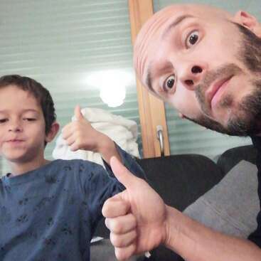 The image shows a man and a boy giving a thumbs-up gesture, with the man\'s face partially visible in the foreground.