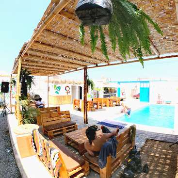 The image depicts a serene outdoor setting with a pool, wooden furniture, and lush greenery, evoking a sense of relaxation and tranquility on a sunny day.