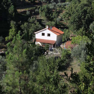 The image depicts a serene white house with a red roof, nestled among lush green trees and bushes, exuding a sense of tranquility and natural beauty.