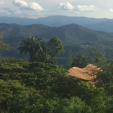 The image depicts a serene landscape featuring a house nestled among lush trees and a majestic mountain range in the background.